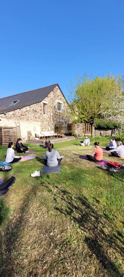 Groupe en méditation assise dans un jardin, devant une longère en pierre, au printemps